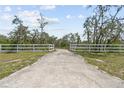 Long private driveway leading to a gated entrance, surrounded by a white fence at 10230 289Th E St, Myakka City, FL 34251