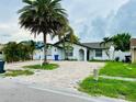 Inviting white home with an arched entryway, a brick driveway, mature trees and lush landscaping at 6806 Monique Ave, Tampa, FL 33625