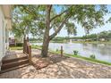 Serene backyard featuring a brick patio and a large tree providing shade overlooking the tranquil lake at 6621 La Mesa Rd, Land O Lakes, FL 34637