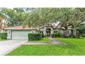 Inviting home featuring a two-car garage, mature trees, lush landscaping, and a green front lawn at 2332 Timbergrove Dr, Valrico, FL 33596