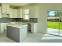 Modern kitchen featuring white cabinets, a gray island, and stainless steel appliances, with backyard views at 13610 Wolfpack Rd, Hudson, FL 34667