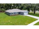 Aerial view of a one-story gray home with stone accents, attached garage, and a green lawn at 11734 Orange Ct, Dade City, FL 33525