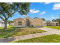 Tan one-story house with a two-car garage and mature landscaping at 28405 Tall Grass Dr, Wesley Chapel, FL 33543