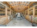 Interior view of a horse barn featuring wooden stalls, a metal roof, and ample space at 8602 State Road 674, Wimauma, FL 33598