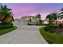 Stunning waterfront home boasts a three-car garage, mature palms, and circular driveway, all set against a colorful sky at 5709 E Longboat Blvd, Tampa, FL 33615