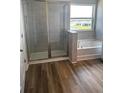 Bathroom with a glass shower enclosure, separate soaking tub, wood-look flooring, and a large window for natural light at 16013 7Th E Ave, Bradenton, FL 34212