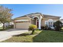 Tan house with red door, two car garage, and landscaped yard at 7720 Rathdown Ln, Wesley Chapel, FL 33545