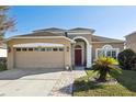 Tan house with red door, two car garage, and landscaped yard at 7720 Rathdown Ln, Wesley Chapel, FL 33545