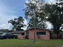 Pink house with a large yard, driveway, and mature trees at 65 Ventura Dr, Dunedin, FL 34698