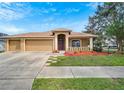 Tan three-car garage home with a red door and nicely landscaped yard at 12739 Standbridge Dr, Riverview, FL 33579