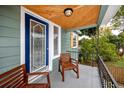 Inviting front porch featuring wood ceiling, seating, a decorative blue front door, and stylish black wrought iron railing at 6619 Livingston N Ave, St Petersburg, FL 33702