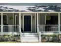 Close up of covered front porch features a stately blue door, steps with potted plants, and hanging plants at 5455 Lake Le Clare Rd, Lutz, FL 33558
