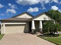 Tan house with beige garage door, landscaping, and palm trees at 13240 Satin Lily Dr, Riverview, FL 33579