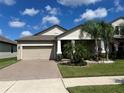 Tan house with beige garage door, landscaping, and palm trees at 13240 Satin Lily Dr, Riverview, FL 33579