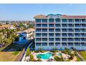 A close exterior view of the condo building with a patio, lawn, and community pool surrounded by palm trees at 17745 Gulf Blvd # 604, Redington Shores, FL 33708