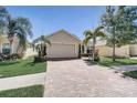 Tan house with brick driveway, palm trees, and manicured landscaping at 1804 Pacific Dunes Dr, Sun City Center, FL 33573