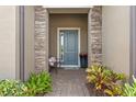 Charming entryway with a blue door, brick pathway, stone pillars, and beautiful potted plants at 26810 Weiskopf Dr, Englewood, FL 34223