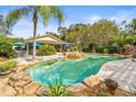 Beautiful backyard pool with mature landscaping, rock waterfall feature, and a covered outdoor living space at 2501 Rustic Oaks Dr, Lutz, FL 33559