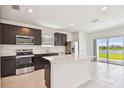 Modern kitchen featuring stainless steel appliances, dark cabinetry, a center island, and sliding glass doors to the exterior at 10533 Hidden Banks Gln, Parrish, FL 34219