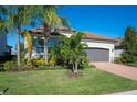 Landscaped one-story home with gray garage door and brick driveway, featuring palm trees and manicured lawn at 12241 Perennial Pl, Bradenton, FL 34211