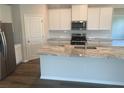 Modern kitchen with white cabinets, a large marble island, stainless steel appliances, and hardwood flooring at 16030 10Th E Ave, Bradenton, FL 34212