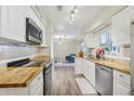 Galley kitchen featuring butcher block countertops, stainless steel appliances, white cabinets, and wood-look flooring at 3407 King George Ln, Seffner, FL 33584