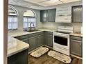 Charming kitchen features gray cabinets, marble countertops, stainless steel sink, arched windows, and wooden floors at 9107 Lingrove Rd, Weeki Wachee, FL 34613