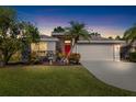 Single-story home with red door, attached garage, and landscaped yard at dusk at 7905 Charing Cross Way, Palmetto, FL 34221