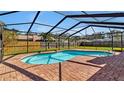 A kidney-shaped pool with brick surround sits in a screened-in enclosure against a wooden privacy fence and blue skies at 7801 17Th N Way, St Petersburg, FL 33702