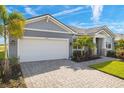 Charming gray home with a two-car garage, brick driveway, and beautifully landscaped front yard with palm trees at 11971 Starbright Path, Venice, FL 34293