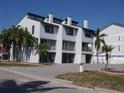 Bright white condo with a paved driveway, balconies, and lush tropical palm trees at 9901 1St E St # F, Treasure Island, FL 33706
