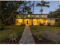 Charming home at dusk with a welcoming front walkway and lit windows, lush lawn, mature palm trees at 323 Coffee Pot Ne Dr, St Petersburg, FL 33704