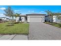 Beautiful single-story home with a gray two-car garage, paver driveway, lush green lawn, and tropical landscaping at 3065 Winding Creek Trl, North Port, FL 34289
