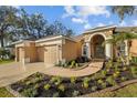 Lovely front yard landscaping leads up to this tan home with a three car garage and covered porch entry at 10101 Paddock Oaks Dr, Riverview, FL 33569