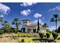 Elegant gated community entrance with white stucco walls, a red tile roof, and lush landscaping against a bright blue sky at 13118 Sorrento Way, Bradenton, FL 34211
