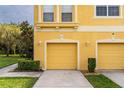 View of two townhouses with yellow siding, two-car garages, and manicured landscaping at 9042 Moonlit Meadows Loop, Riverview, FL 33578