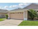 A light brown two-car garage attached to the residence with green grass and a palm tree at 31447 Shaker Cir, Wesley Chapel, FL 33543