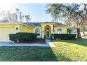 Inviting one-story home featuring a vibrant yellow exterior, lush landscaping, and a welcoming arched entryway at 5215 New Brittany Ln, Zephyrhills, FL 33541