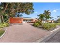Charming single-story home featuring a lush landscaped yard, brick driveway, and solar panels on the roof at 5166 39Th S St, St Petersburg, FL 33711