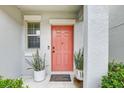 Inviting front entrance with a coral door, potted plants, a welcome mat, and a window on the side at 13456 Marble Sands Ct, Hudson, FL 34669