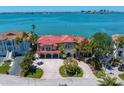 Waterfront home featuring a red tile roof, lush landscaping, and situated near bay waters and a distant city skyline at 26 Sunset Bay Drive, Belleair, FL 33756