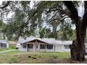 A quaint one-story home with a covered porch, and a large tree offering shade in the front yard, in need of repair at 34799 Evergreen Way, Dade City, FL 33523