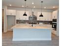 Modern kitchen with white cabinets, gray backsplash, stainless hood, and a large island with pendant lighting at 695 Allora Ave, Nokomis, FL 34275