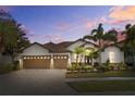 Inviting home exterior with a three car garage, paver driveway, lush landscaping, and exterior lighting at 1893 Riveredge Dr, Tarpon Springs, FL 34689