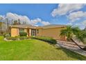 Single Gathering home showcasing lush lawn, colorful palm tree, shrubbery, and light colored exterior with dark shutters at 1123 Emerald Dunes Dr, Sun City Center, FL 33573