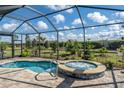 A screened in pool with a spa sits on a brick patio surrounded by grass and shrubbery at 4748 Ballast Crest Cv, Land O Lakes, FL 34638