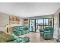 Spacious living room filled with comfortable green couches, a chair, and a view out to the balcony at 800 S Gulfview Blvd # 403, Clearwater Beach, FL 33767