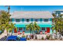 Bright turquoise coastal duplex with red doors, white picket fence, and lush palm trees in a sunny setting at 308 2Nd St N # 202, Bradenton Beach, FL 34217