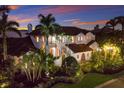 Stunning Mediterranean-style home with a tile roof and lush tropical landscaping at twilight at 705 Riviera Dunes Way, Palmetto, FL 34221