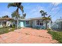 Charming light blue single story home featuring a sunny yellow door, complemented by lush palm trees at 14105 E Parsley Dr, Madeira Beach, FL 33708